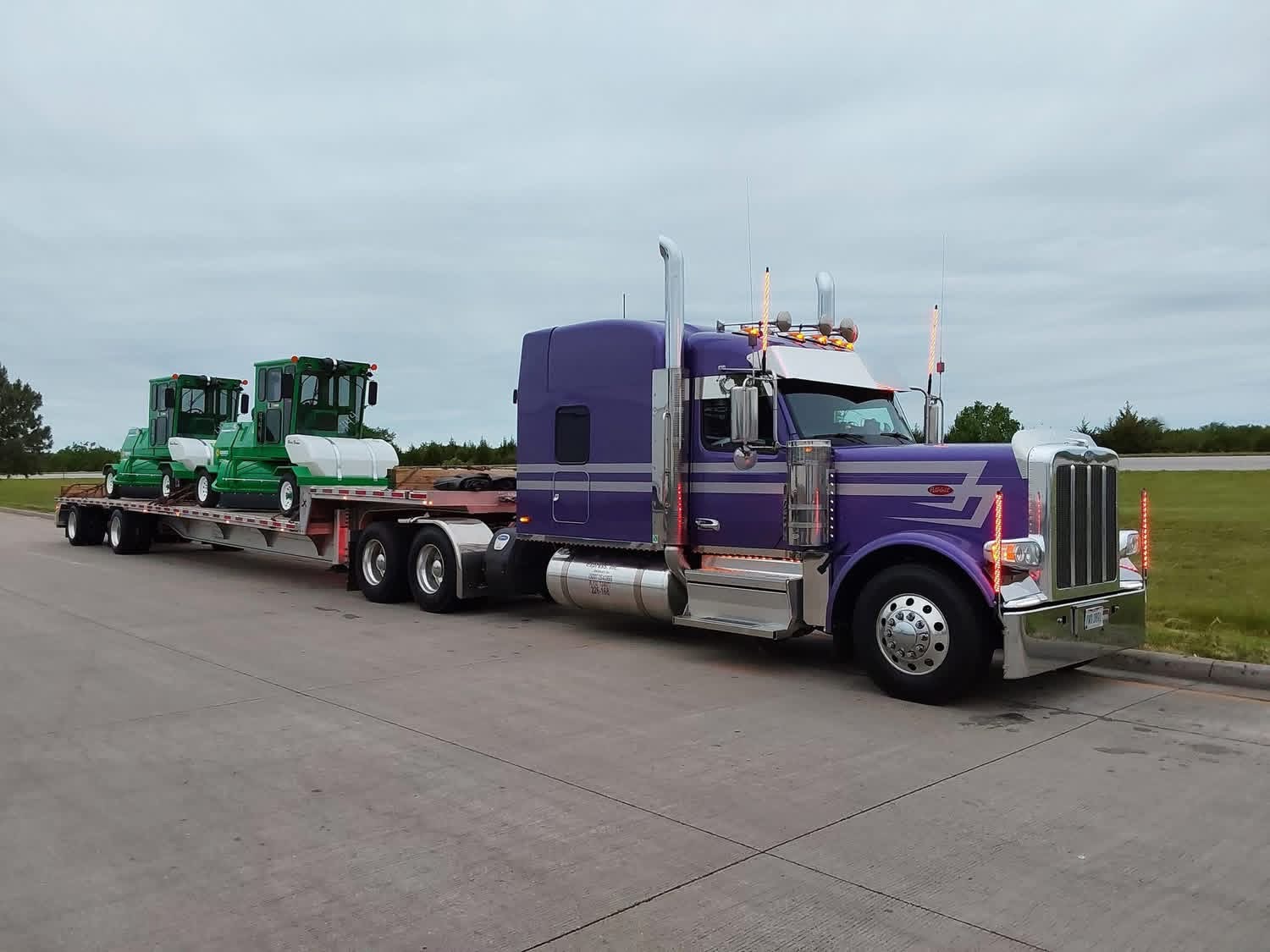 Purple Peterbilt flatbed hauling two green industrial tractors